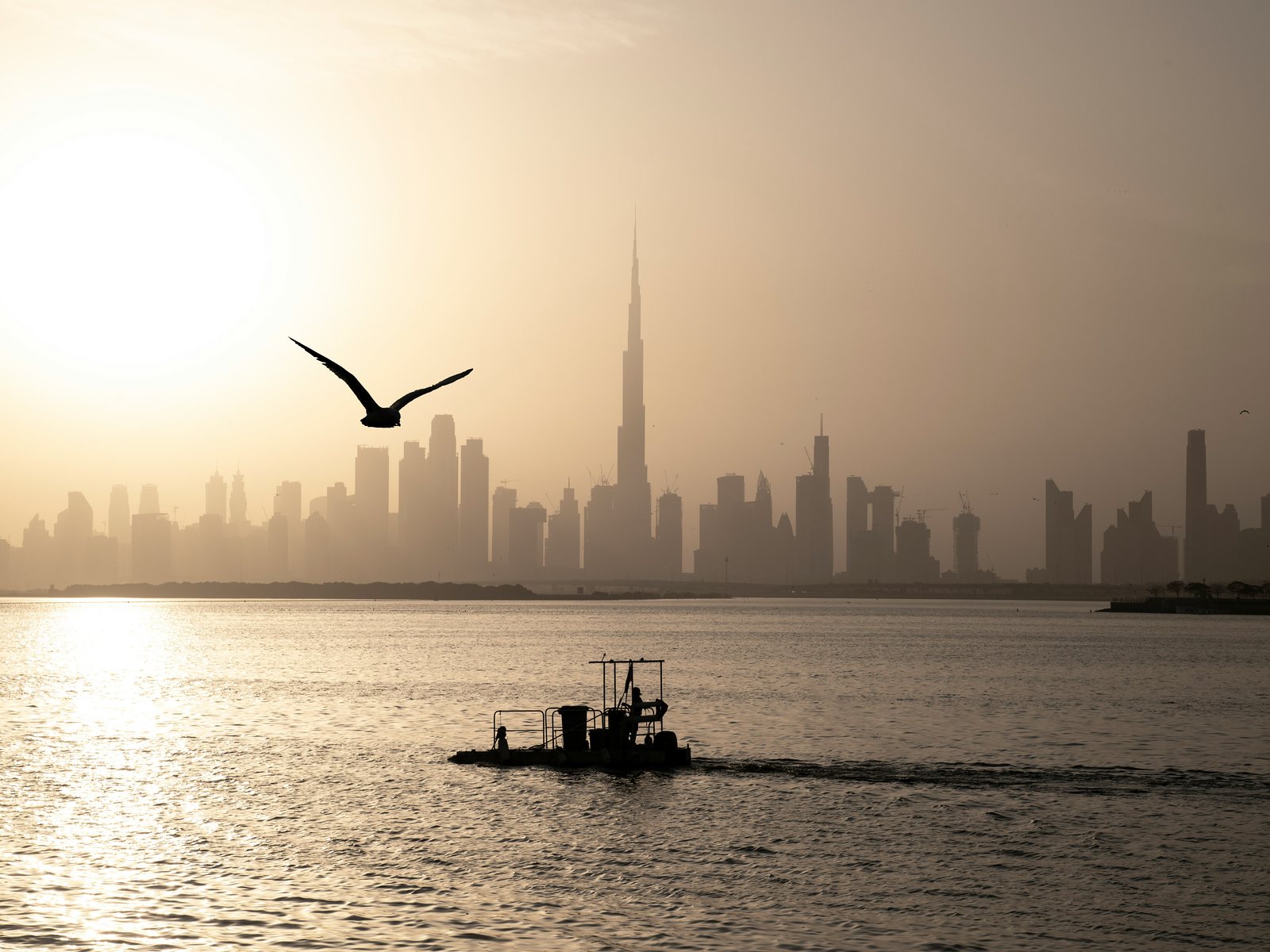The Dubai skyline at dawn across the water, with a small boat in the foreground